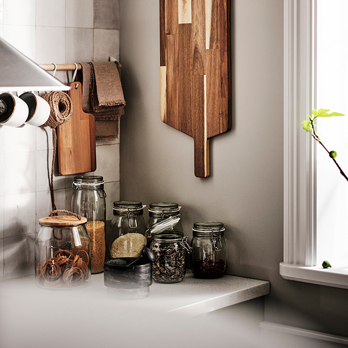 Encimera de cocina con frascos KORKEN que almacenan productos secos, tablas de cortar de madera y toallas. Frascos sellados para preservar la frescura.