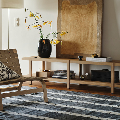 Sala de estar luminosa con alfombra gris con estampado de abedul, mesa de centro de madera, jarrón negro con flores amarillas, silla de mimbre y gran arte abstracto en la pared.