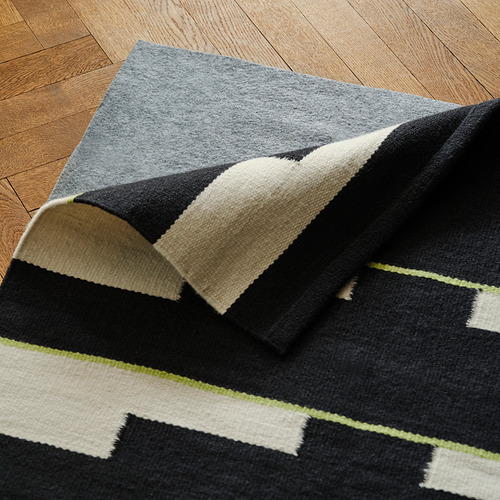 Alfombra geométrica de lana expuesta sobre suelo de madera, con patrón reversible.