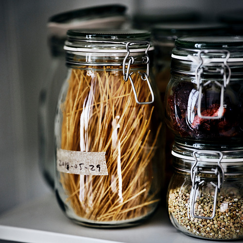 Tres frascos de vidrio con abrazaderas de metal almacenan fideos secos y semillas, sellados para mayor frescura.