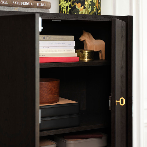 Un elegante armario con estantes ajustables que exhiben libros y decoración. Cerradura de latón visible en la puerta.