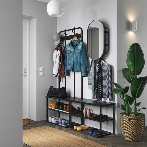 Entrada bien organizada con zapatero NIPÅSEN negro, percheros y espejo. Alfombra de madera y planta en maceta.