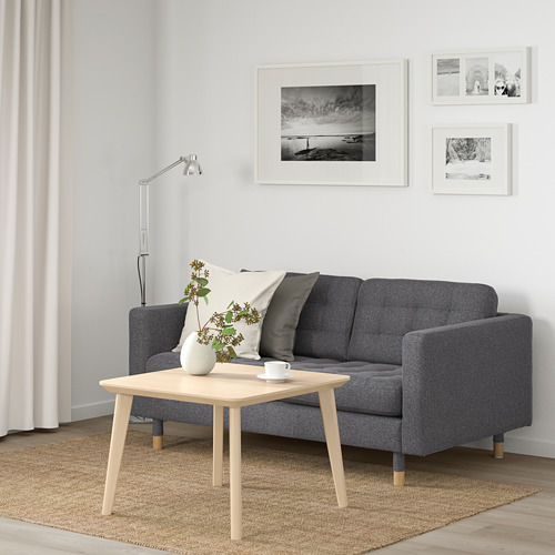 Espacio habitable minimalista con sofá LANDSKRONA gris, mesa de centro de madera y arte de pared en blanco y negro. Las cortinas enmarcan la ventana, añadiendo calidez.
