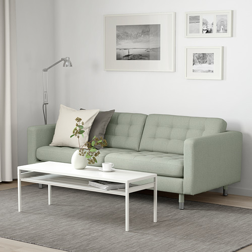 Sofá verde LANDSKRONA de 3 plazas con almohadas, arte de pared, mesa de centro, jarrón y taza.