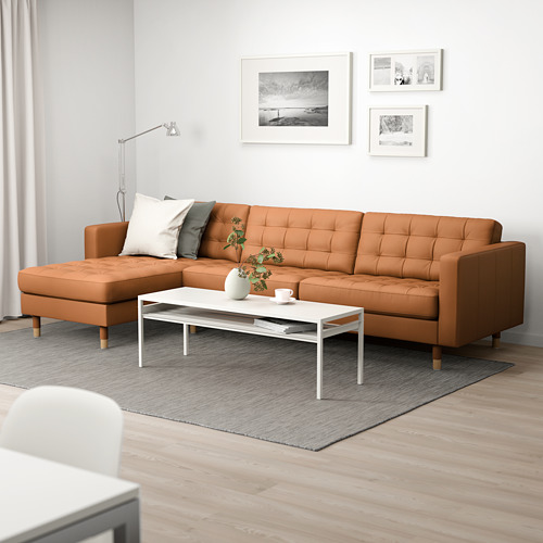 Sala de estar moderna con sofá seccional de color marrón anaranjado, mesa de café, jarrón y fotos. Iluminado por luz natural y lámpara.