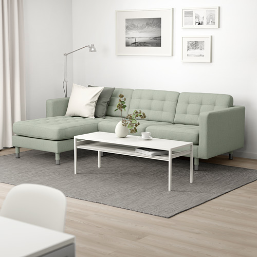Sofá LANDSKRONA verde de 3 plazas con tumbona en salón moderno, alfombra gris, mesa de centro blanca con decoración.