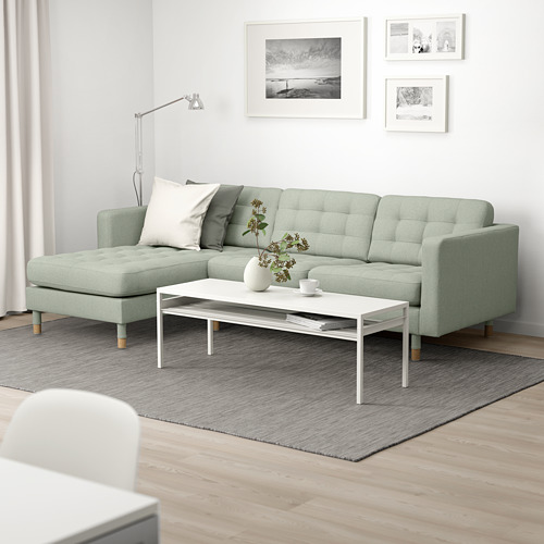 Una sala de estar moderna con un sofá skrona verde menta, una mesa de centro blanca, fotos en blanco y negro y una alfombra gris.