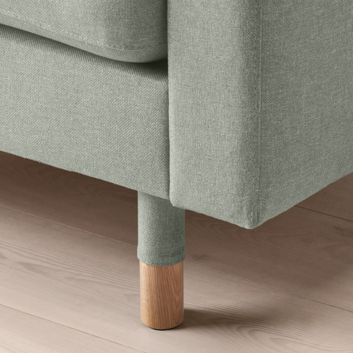 Primer plano de una pata de sofá tapizada de color verde claro suave sobre suelo de madera.