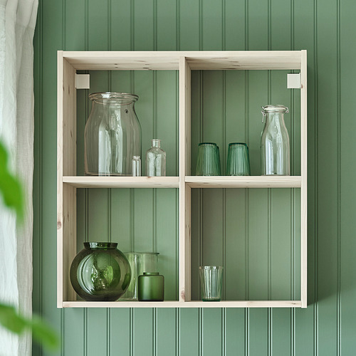 Estante de pared con frascos de vidrio transparente y verde en compartimentos contra la pared verde.