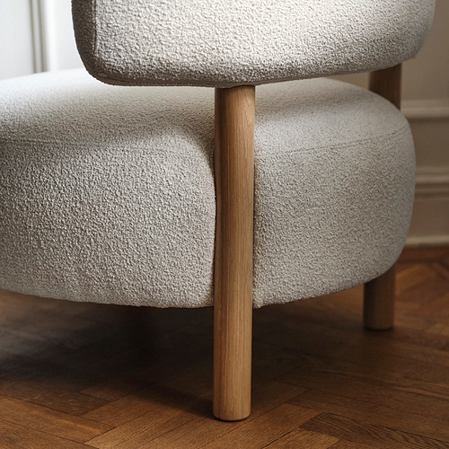 Un sillón gris claro con patas de madera. La tapicería suave y redondeada crea una experiencia de asiento cómoda.