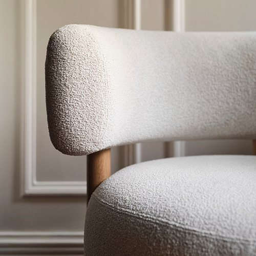 Primer plano de una silla moderna y de alta calidad. La tela suave y texturizada cubre el respaldo y el asiento de felpa, sobre patas de madera maciza.