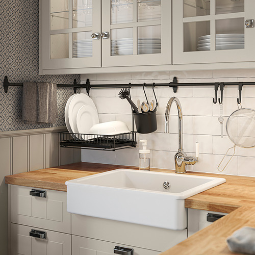 Fregadero de cocina, de madera y blanco. Soporte para limpiador negro. Escurreplatos. Las vitrinas muestran los platos.