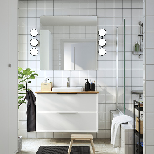 Baño moderno con encimera de bambú ÅLSKEN, lavabo, espejo y ducha. Puerta de vidrio, taburete y planta pequeña.