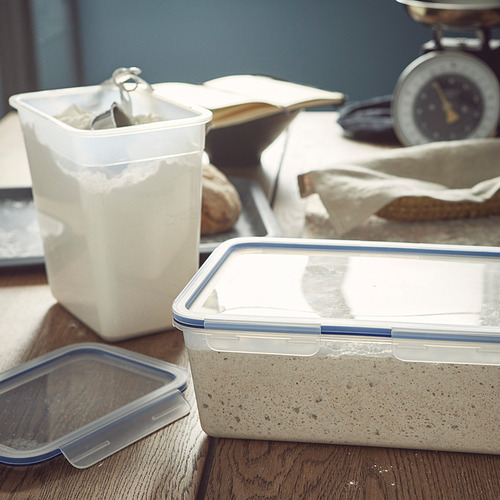 Recipientes de plástico transparente con tapas azules, uno que contiene avena y otro cubierto, se asientan sobre una superficie de madera, ideales para almacenar y transportar alimentos secos.