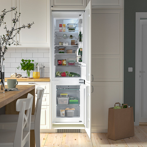 Nevera/congelador integrado abierto con estantes ajustables, que revelan productos frescos y bebidas, en una cocina moderna.