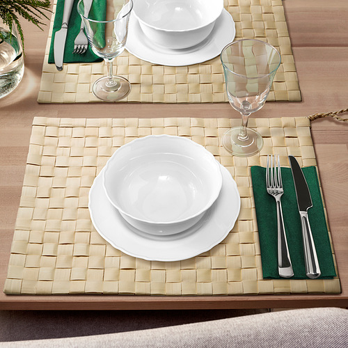 Manteles individuales MÄVINN beige con diseño de hojas de palma, con platos y vasos blancos, servilletas verdes, mesa caliente.