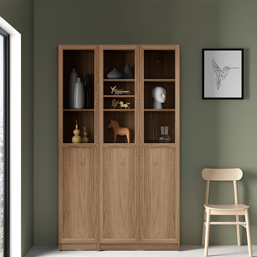 Gran librería de madera BILLY contra la pared verde, con jarrones y figuritas. Silla del lado derecho y arte de pared visibles.
