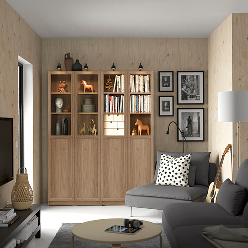 Sala de estar con una gran estantería de madera BILLY llena de libros y decoración. Sofá gris, mesa de centro y fotos enmarcadas colgantes. Guitarra en la pared.