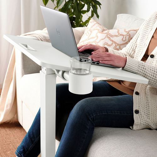 Persona que usa una mesa portátil ajustable con bebida, en un sofá acogedor.