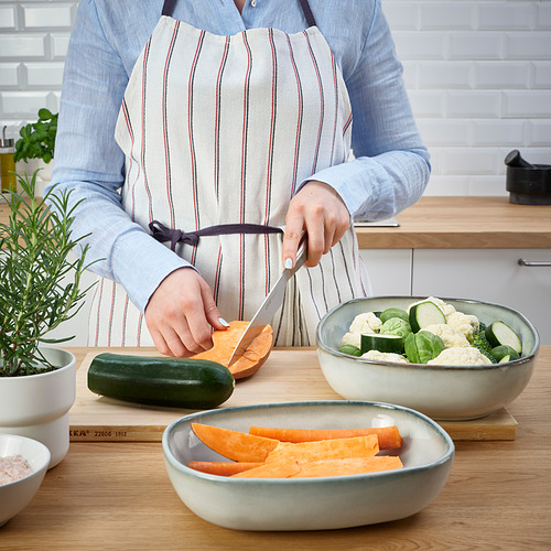 Persona cortando verduras al lado de tazones. Plato utilizado para servir alimentos directamente del horno a la mesa.