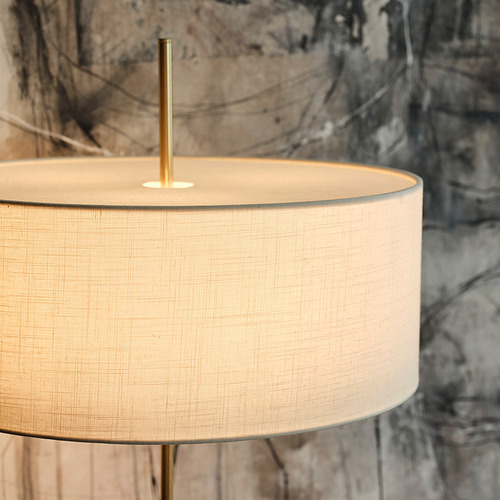 Una lámpara moderna con una base de color latón y una pantalla beige texturizada se asienta sobre una base de travertino. Diseño elegante, materiales de calidad.