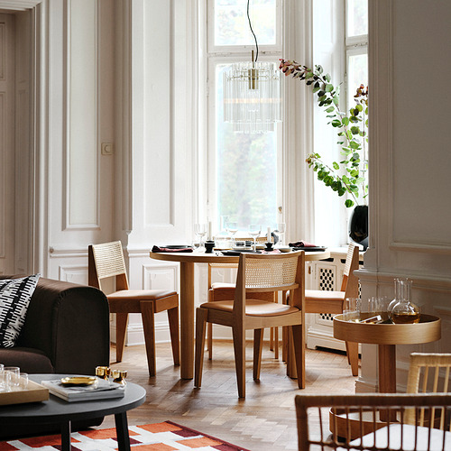 Comedor moderno con mesa de madera, sofá oscuro, gran ventanal y elegante candelabro.