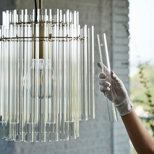 La mano enguantada ajusta el candelabro de latón con tubos de vidrio por una ventana grande.
