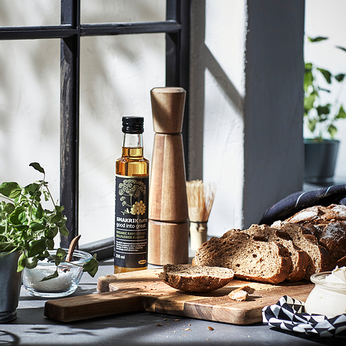Molinillo de pimienta de madera cerca de la ventana de la cocina con pan y plantas.