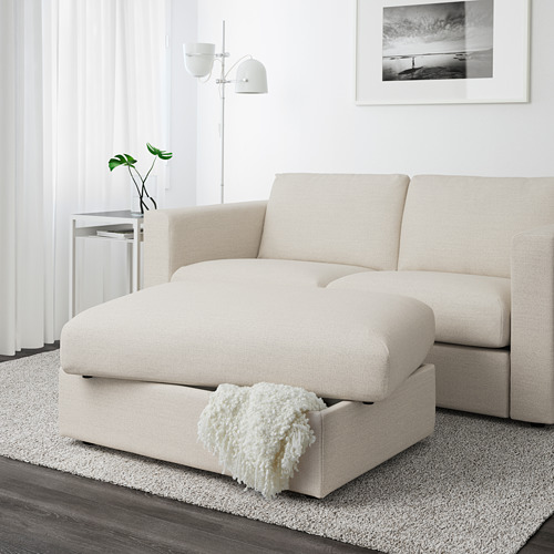 Sala de estar moderna con sofá seccional VIMLE beige con una otomana con almacenamiento, cubierta con una manta blanca con flecos.