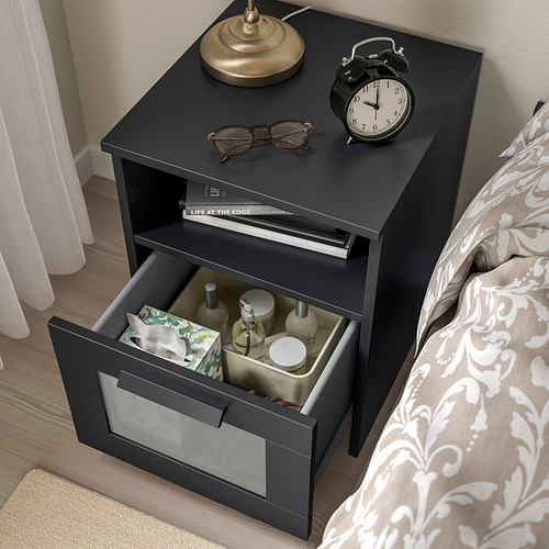 Mesita de noche negra, cajón abierto, lámpara, reloj, etc. Serie BRIMNES para dormitorio.