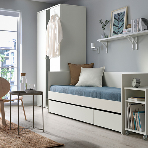 Dormitorio moderno con sofá cama blanco, cojines azules, estanterías, silla y estantería.