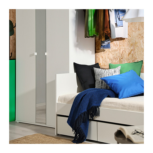 Dormitorio moderno con sofá cama VIHALS blanco, manta azul, almohadas de colores, cajones grises y perchero.
