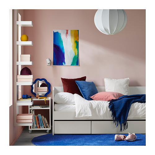 Dormitorio moderno con un sofá cama blanco, decoración azul y blanca, obras de arte coloridas y una estantería móvil.