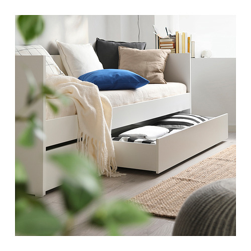 Moderno sofá cama blanco con cajones, ropa de cama elegante, almohadas acogedoras y una manta acogedora, perfecta para dormir o descansar.