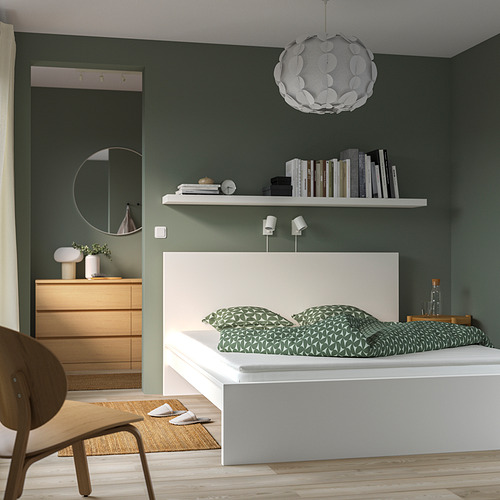 Dormitorio con almohadilla NÄSFJÄLLET verde, edredón estampado, estantería, silla y lámpara colgante.
