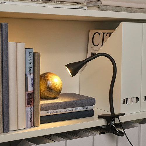Estantería con una lámpara de lectura de pina, que ilumina una pila de libros. Iluminando los libros con una luz cálida, creando un ambiente acogedor para la lectura.