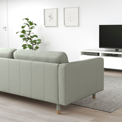 Sala de estar minimalista moderna con sofá LANDSKRONA verde claro, patas de madera, mueble de TV blanco, televisor negro y arte de pared.