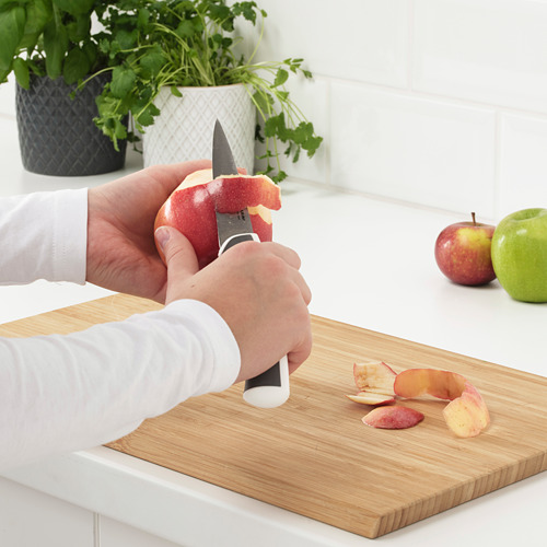 Persona pelando manzana con cuchillo de ÄNDLIG colocado en tabla de cortar de madera.
