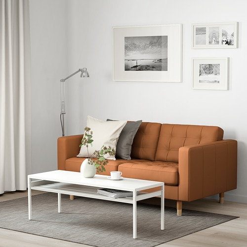 Sala de estar moderna con sofá marrón, almohadas, mesa de centro con elementos contra la pared blanca con fotos.