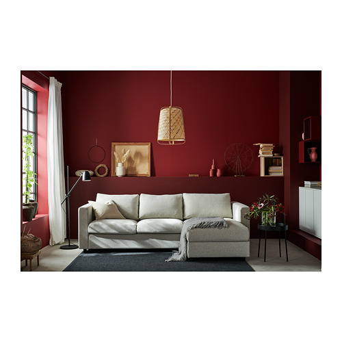 Salón moderno con paredes rojas, sofá VIMLE gris claro, lámpara boho, cortinas blancas y elementos decorativos.