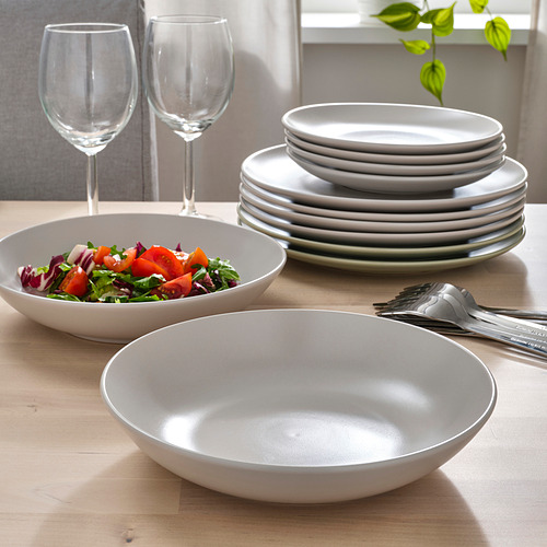 Mesa puesta con platos de color gris claro: platos apilados, cuencos rellenos de ensalada y vacíos. Copas de vino y cubiertos incluidos.