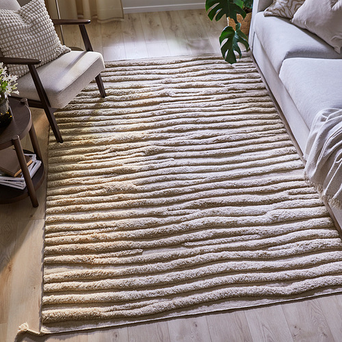 Una alfombra de lana tejida a mano, a rayas y gris claro en una sala de estar con un sofá y una silla.