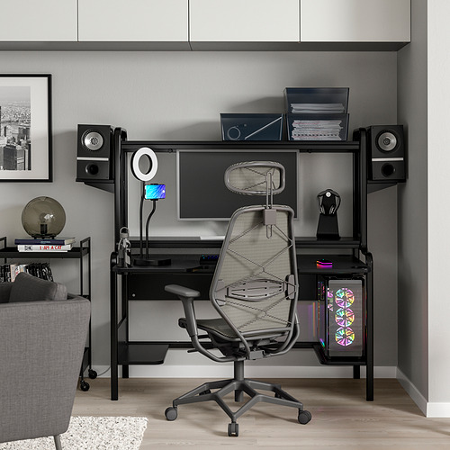 Moderna configuración de oficina en casa negra con un elegante escritorio, una silla ergonómica de malla y rodeada de dispositivos de alta tecnología.