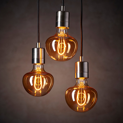 Tres bombillas de estilo vintage cuelgan y emiten un cálido resplandor ámbar; En forma de campana con filamentos expuestos.