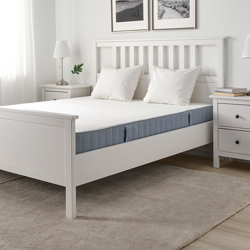 Dormitorio minimalista con colchón VESTMARKA blanco, dos almohadas, mesitas de noche con lámparas, libros y plantas, alfombra.