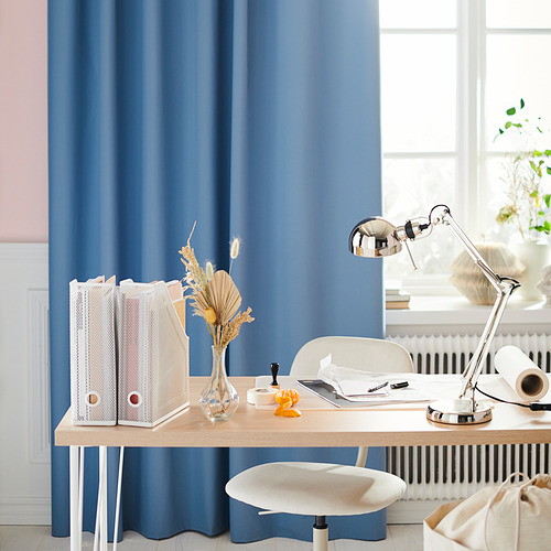 Moderna oficina en casa con cortinas azules, escritorio de madera, silla blanca y lámpara FORSÅ plateada ajustable.