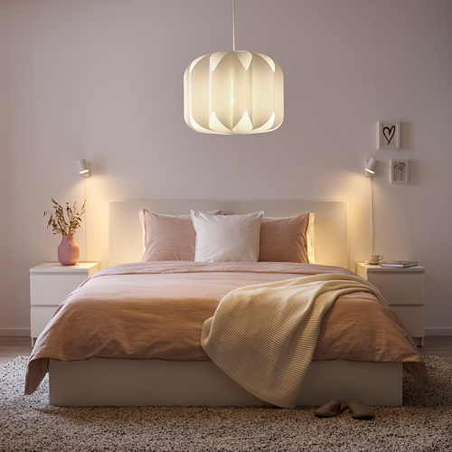 Dormitorio acogedor: cama central, luces cálidas, almohadas rosas, decoración en mesitas de noche, paredes suaves, alfombra, zapatillas, luz colgante.