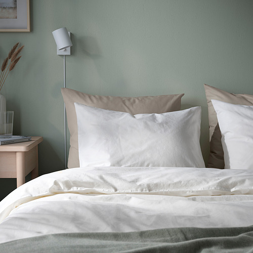 Fundas de almohada blancas DVALA y ropa de cama sobre colchón, luz de pared, mesita de noche pequeña con vidrio, decoración. Algodón suave y natural.