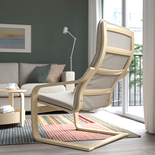 Un elegante sillón de madera clara con un cojín beige cerca de una ventana, junto a una alfombra de colores en una acogedora sala de estar.