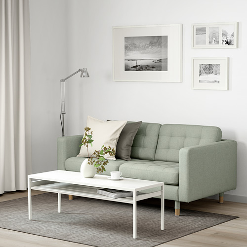 Moderno salón con sofá verde de 2 plazas, mesa de centro blanca, lámpara y alfombra de rayas.